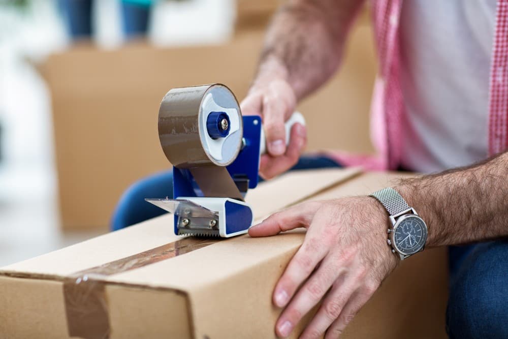 Hands running a tape gun along the seam of a packed kit box