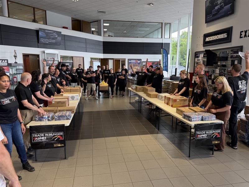 Kunes staff lined up along two packing tables under Trade in Hunger banners