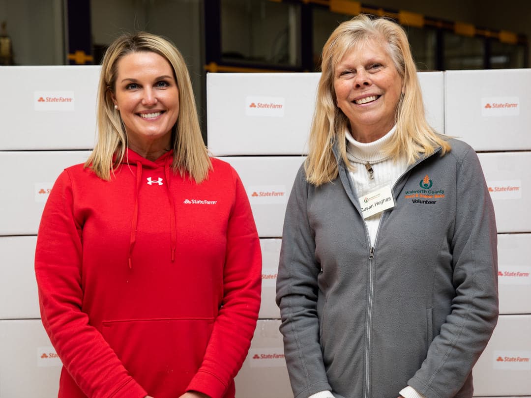 A State Farm agent and a pantry volunteer in front of stacked kit boxes