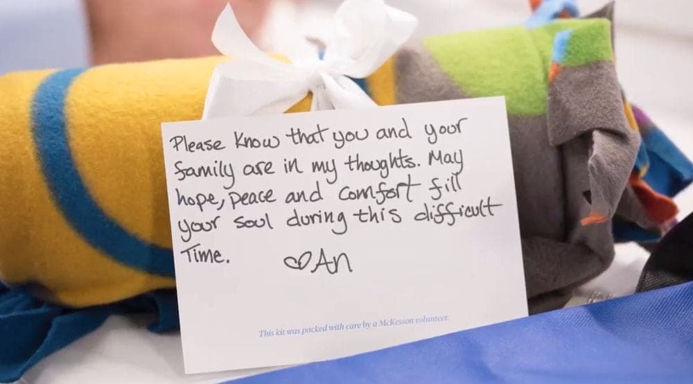 A rolled fleece blanket tied with ribbon beside a hand-written note to the recipient