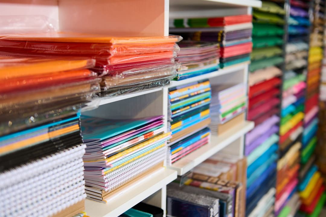 Shelves stacked with notebooks, folders and construction paper sorted by color